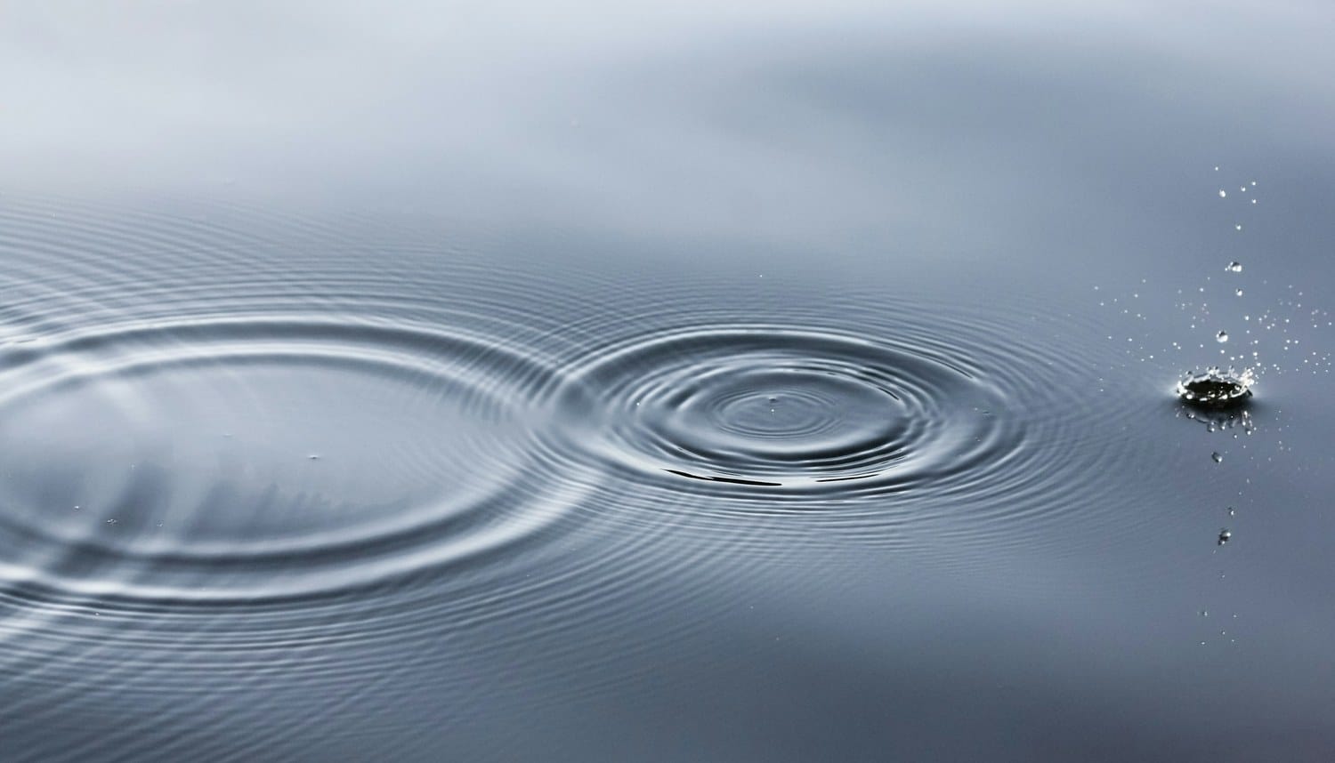 Concentric ripples spreading outward across the surface of still, pale blue water.
